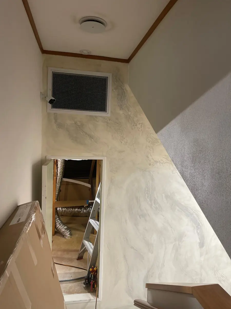 A return-air grille installed high in a stairwell wall during a ducted installation