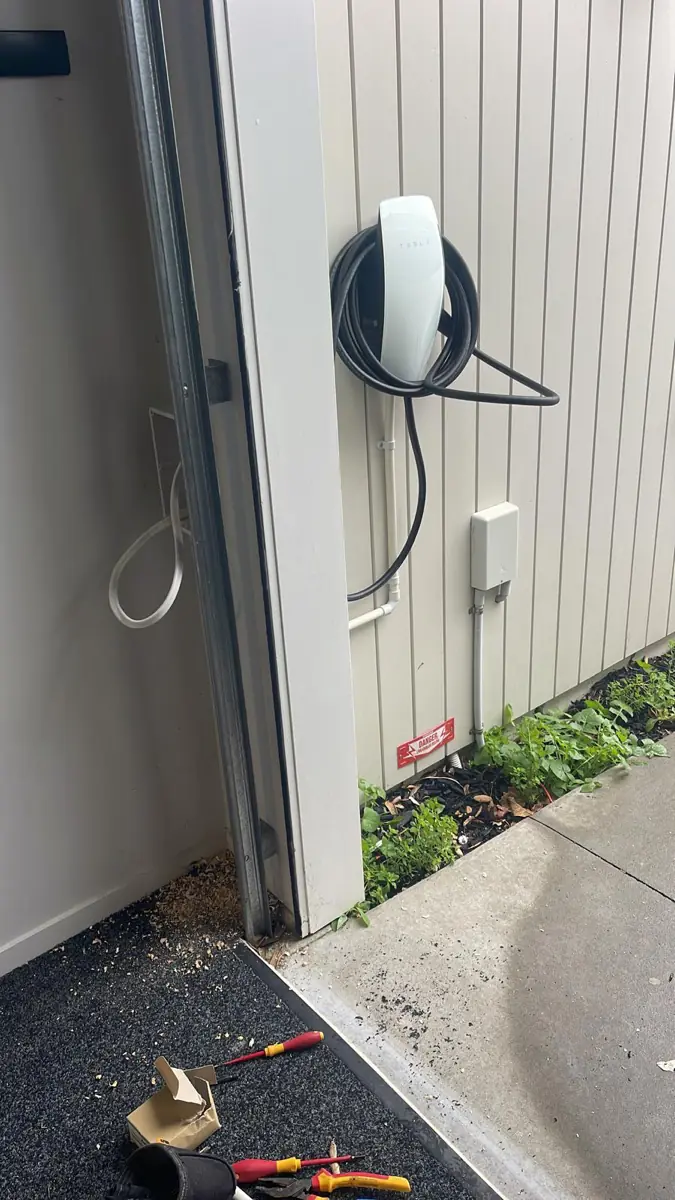 A wall-mounted EV charger installed beside a garage door with its isolating switch