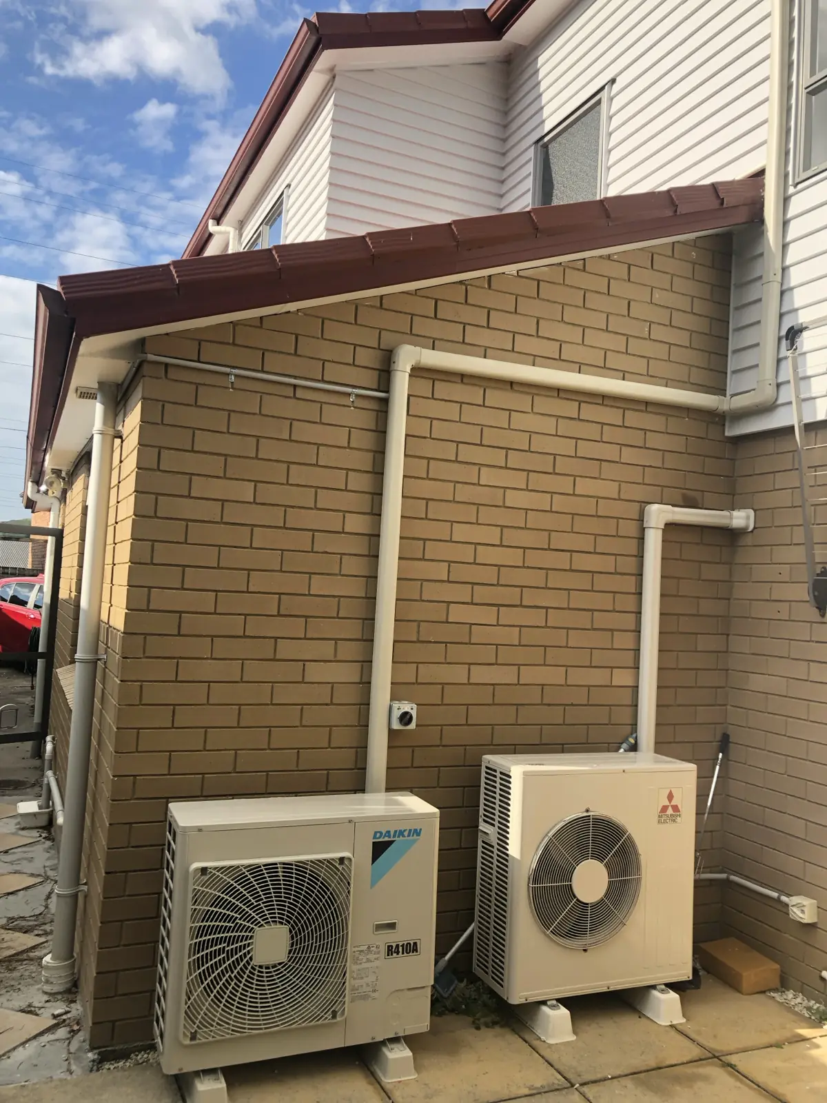 Two heat pump outdoor units mounted on a brick wall with tidy pipework runs