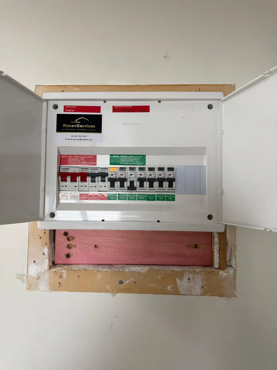 A completed switchboard replacement recessed into the wall with red and green compliance labels